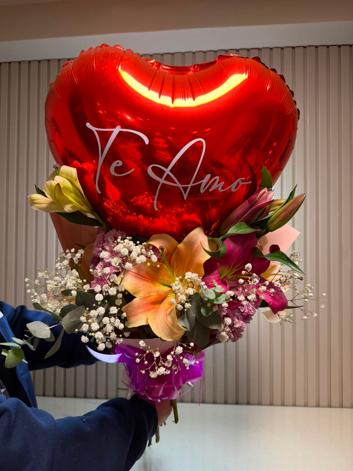 Globo rojo en forma de corazón con la inscripción “Te Amo” sobre un colorido ramo de flores en el interior.