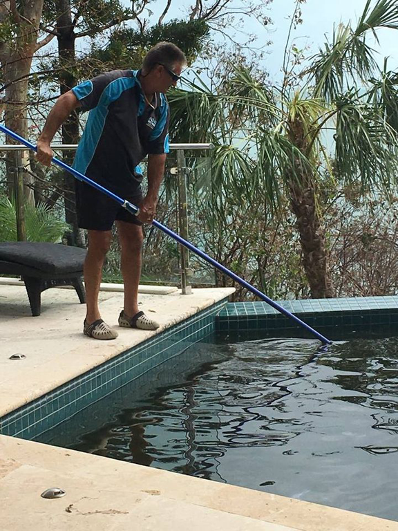 Person Skims Debris From a Pool With a Long Net Beside a Patio and Potted Plants — Focus On Water In Arlie Beach, QLD