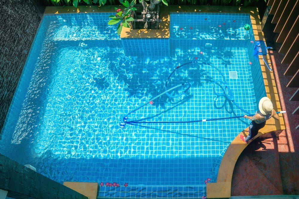 A Woman is Cleaning a Swimming Pool With a Vacuum Cleaner —  Focus On Water In Cannonvale, QLD