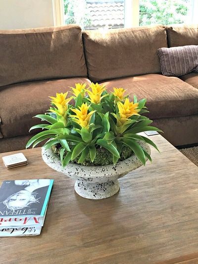 A vase of yellow flowers is sitting on a wooden table in a living room.