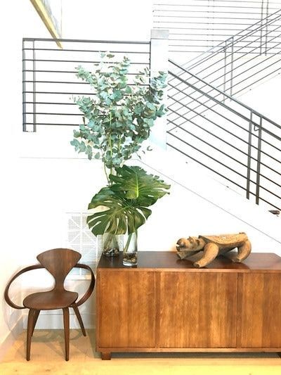 A wooden dresser with a plant and a chair in front of a staircase.