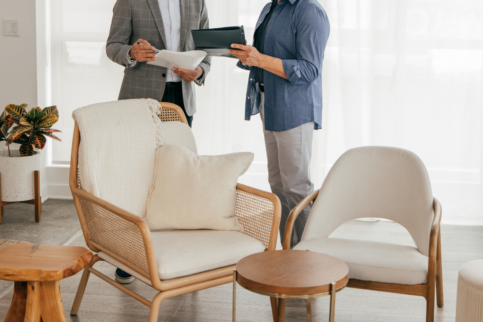 Two people discussing papers in a bright living room with cream chairs and small wooden tables