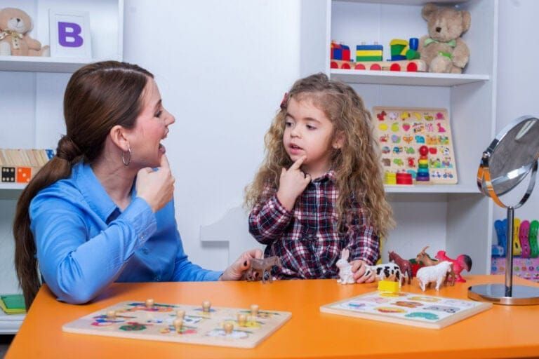Speech therapist working with a young child. They are practicing mouth movements with toys nearby.