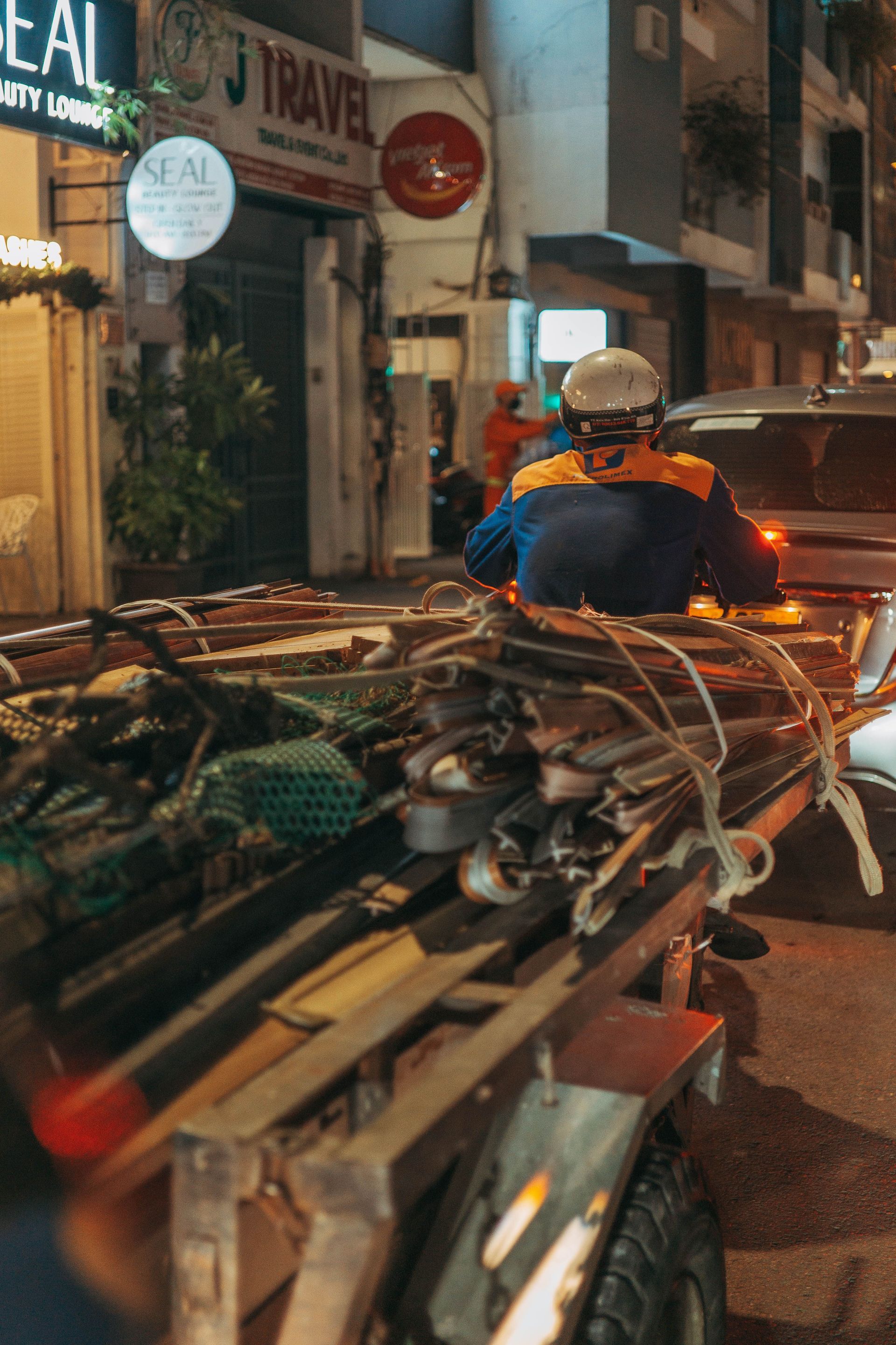 Motorbike parked on a narrow nighttime street beside storefronts, with cluttered cargo in the foreground