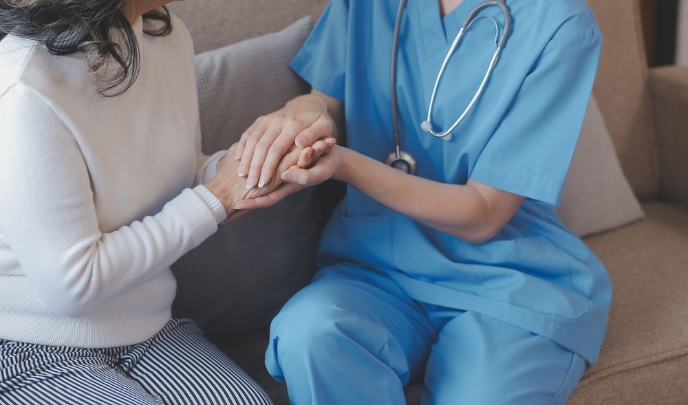 Doctor in blue scrubs holding a patient’s hands on a couch, offering comfort and support
