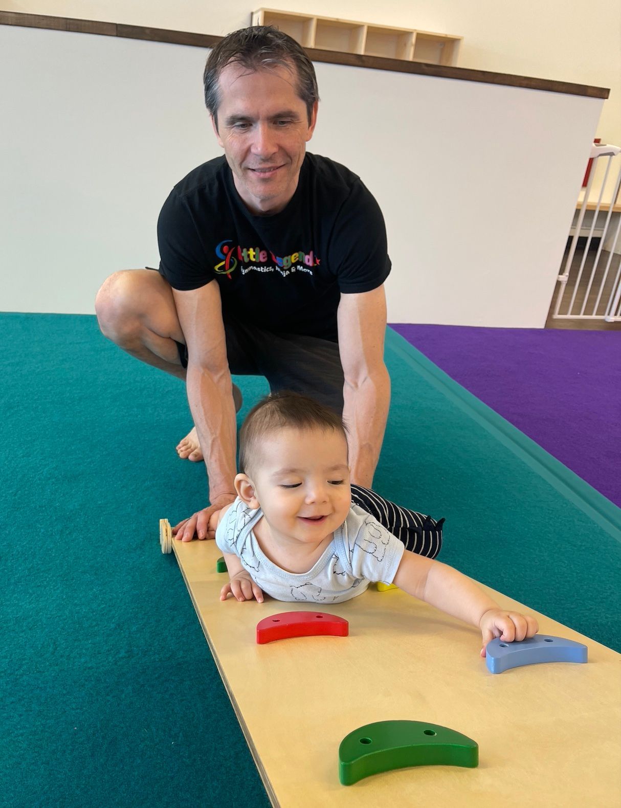 Woman lying on floor, holding up a smiling child in a yellow shirt.