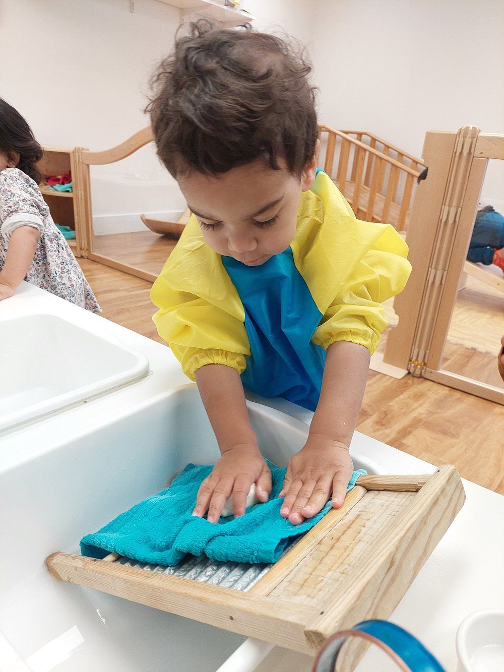 A young boy is washing a towel on a wooden washboard.