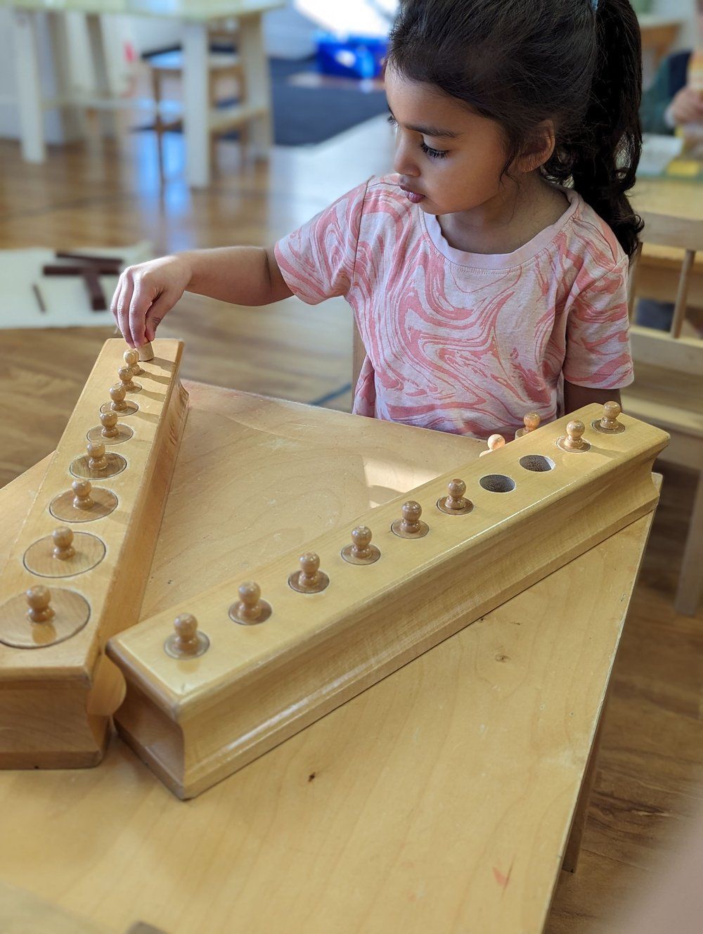 A little girl is playing with a wooden toy on a table.