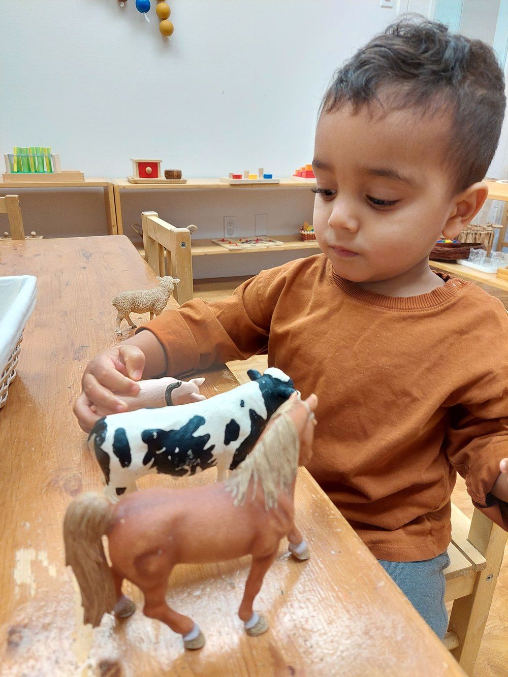 A young boy is sitting at a table playing with a cow and a horse.