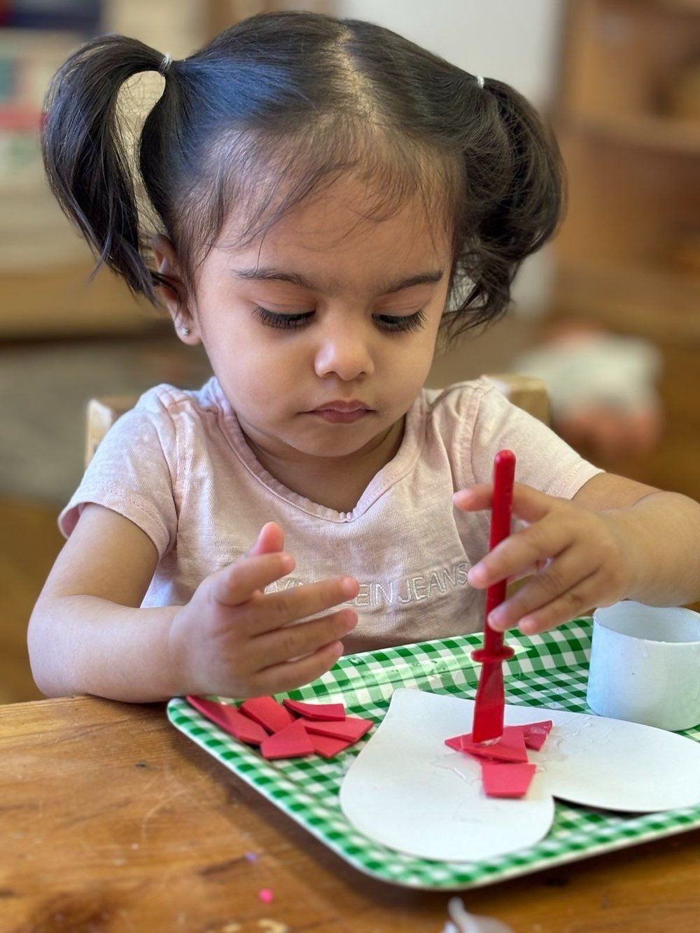 A little girl is sitting at a table making a snowman out of paper.