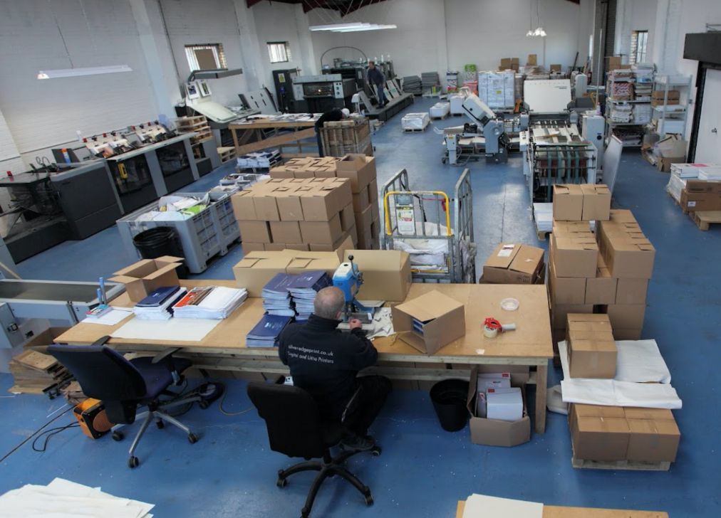 A man sits at a desk in a warehouse surrounded by boxes