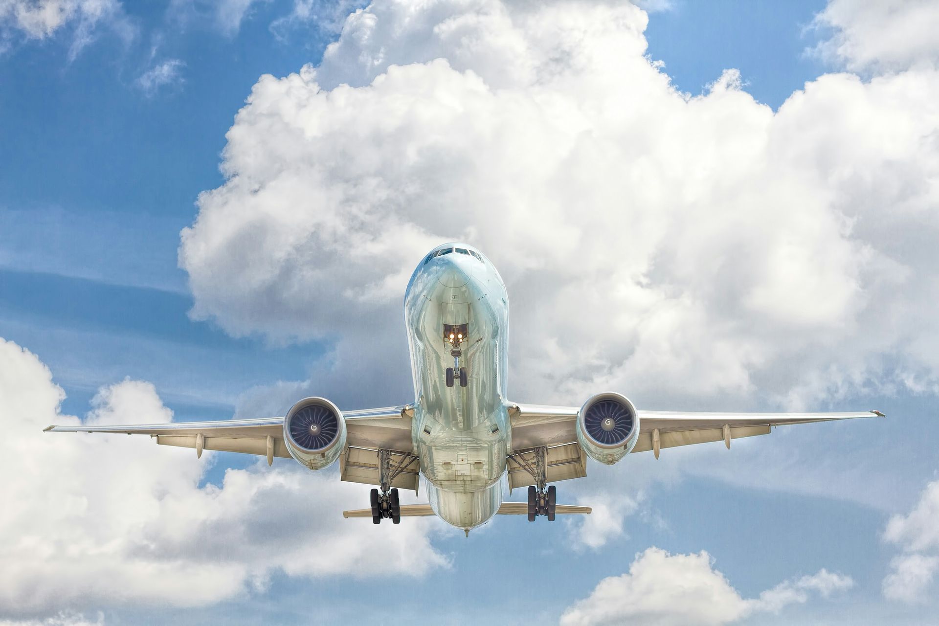Airplane descending with landing gear down against a bright cloudy sky