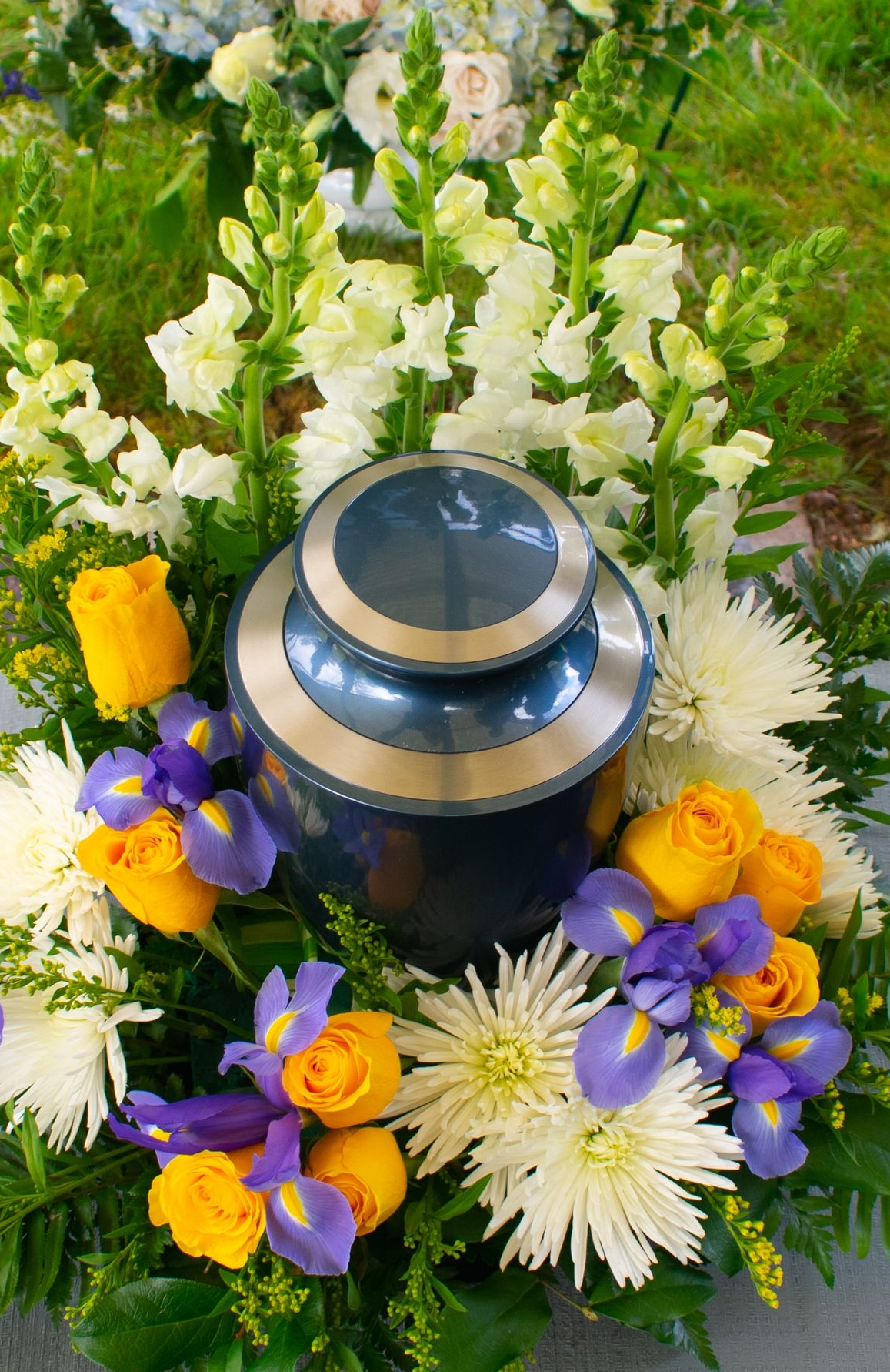Silver memorial urn surrounded by yellow, white, and purple flowers on grass