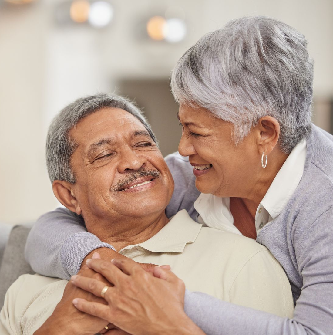 Smiling older couple embracing indoors, with gray hair and warm expressions.