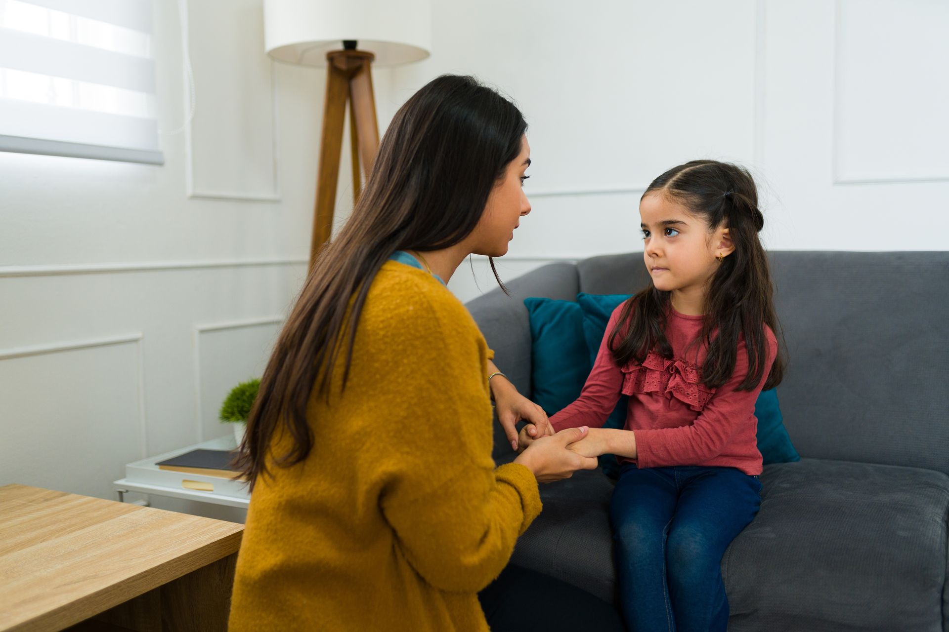 Woman speaking gently with a child on a couch in a bright living room