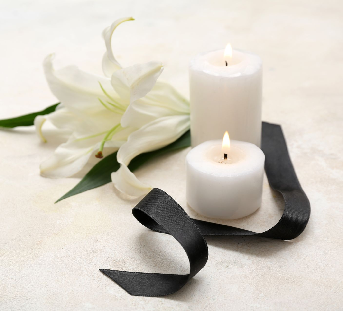 White lilies with two lit white candles and black ribbon on a soft cream background