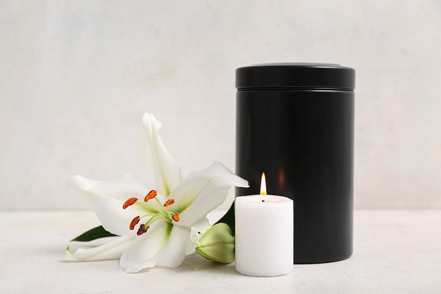 White lily and lit candle beside a black cylindrical container on a white surface