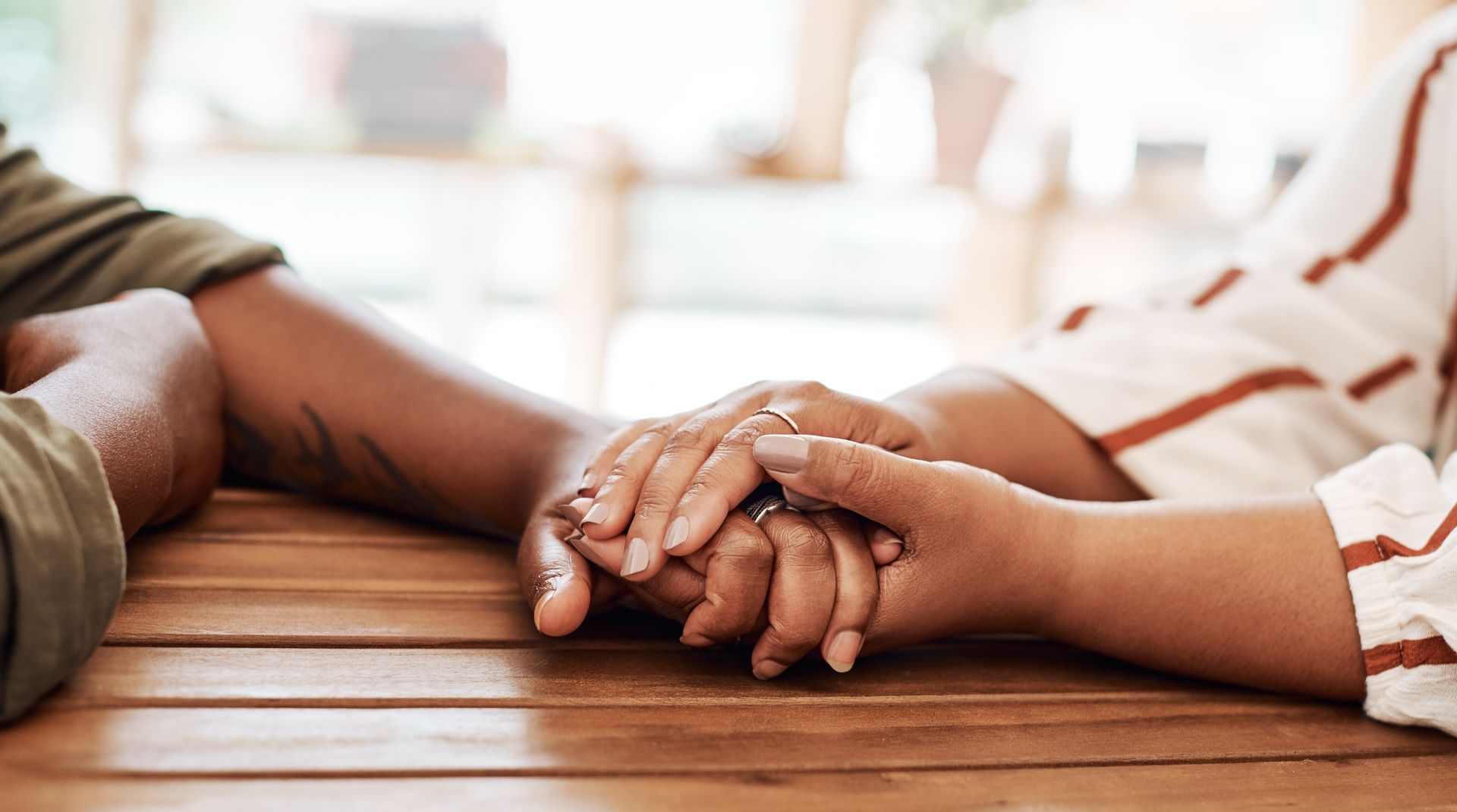 Two hands gently clasped on a wooden table, with a soft blurred background