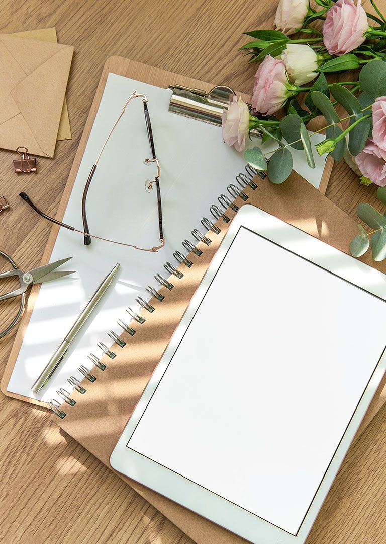 Notebook and eyeglasses on a wooden desk with flowers and stationery