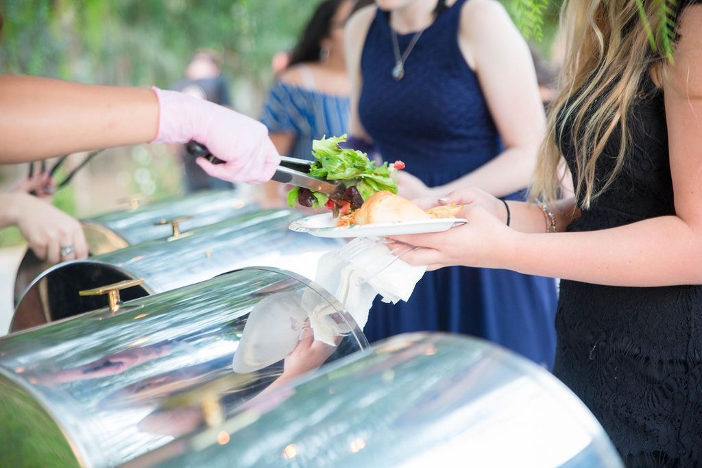 Person receiving food from a buffet server. Salad and wrap being served from a silver warmer.
