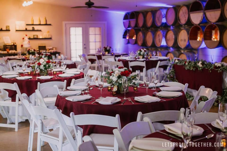 Wedding reception with round tables set with burgundy linens, white chairs, and floral centerpieces