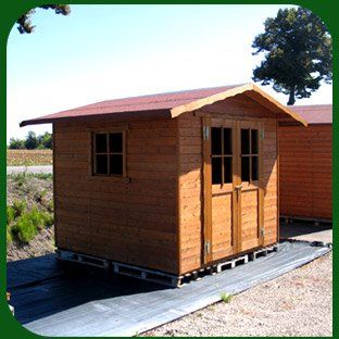 Piccola casetta di legno con tetto rosso su una base pavimentata, all'aperto in un contesto rurale.