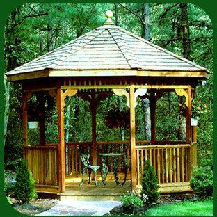 Gazebo da giardino in legno con tetto di tegole, immerso tra alberi e fiori rigogliosi.