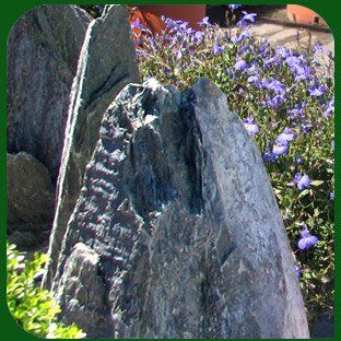 Un'alta lastra di pietra grigia in un giardino con fiori viola sullo sfondo.