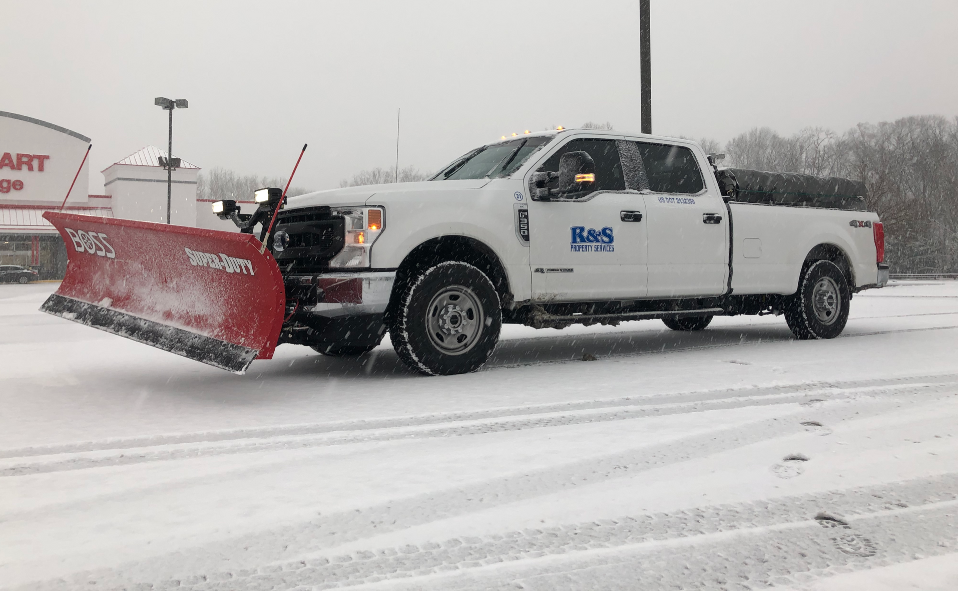 White truck with plow clearing snow in parking lot, snowy conditions. 