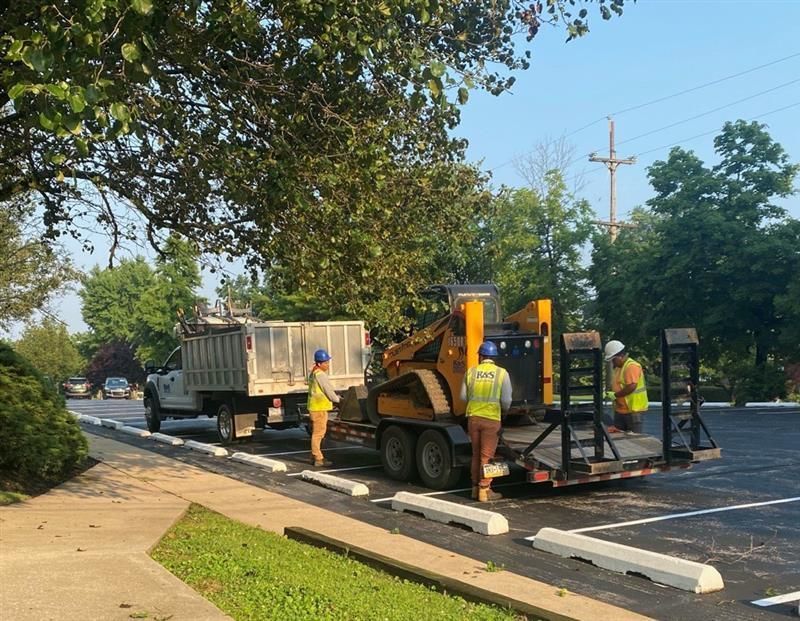 Workers with a wood chipper and truck, parked on asphalt, chipping tree branches.