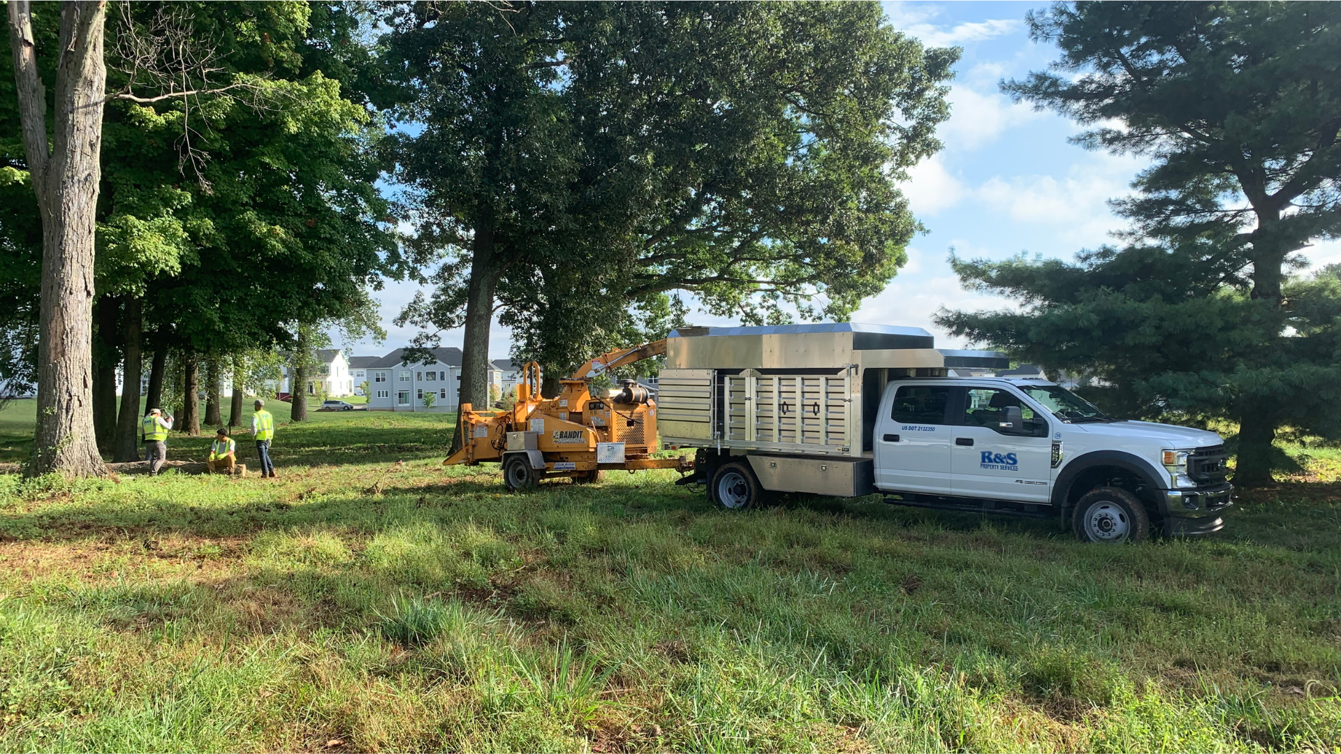 Tree service crew with truck and chipper in grassy area.