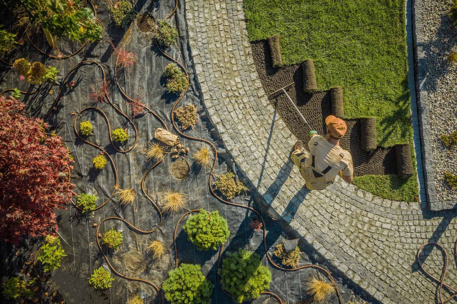Overhead view of a person laying sod rolls near a cobblestone path in a landscaped garden by R&S Property Services.