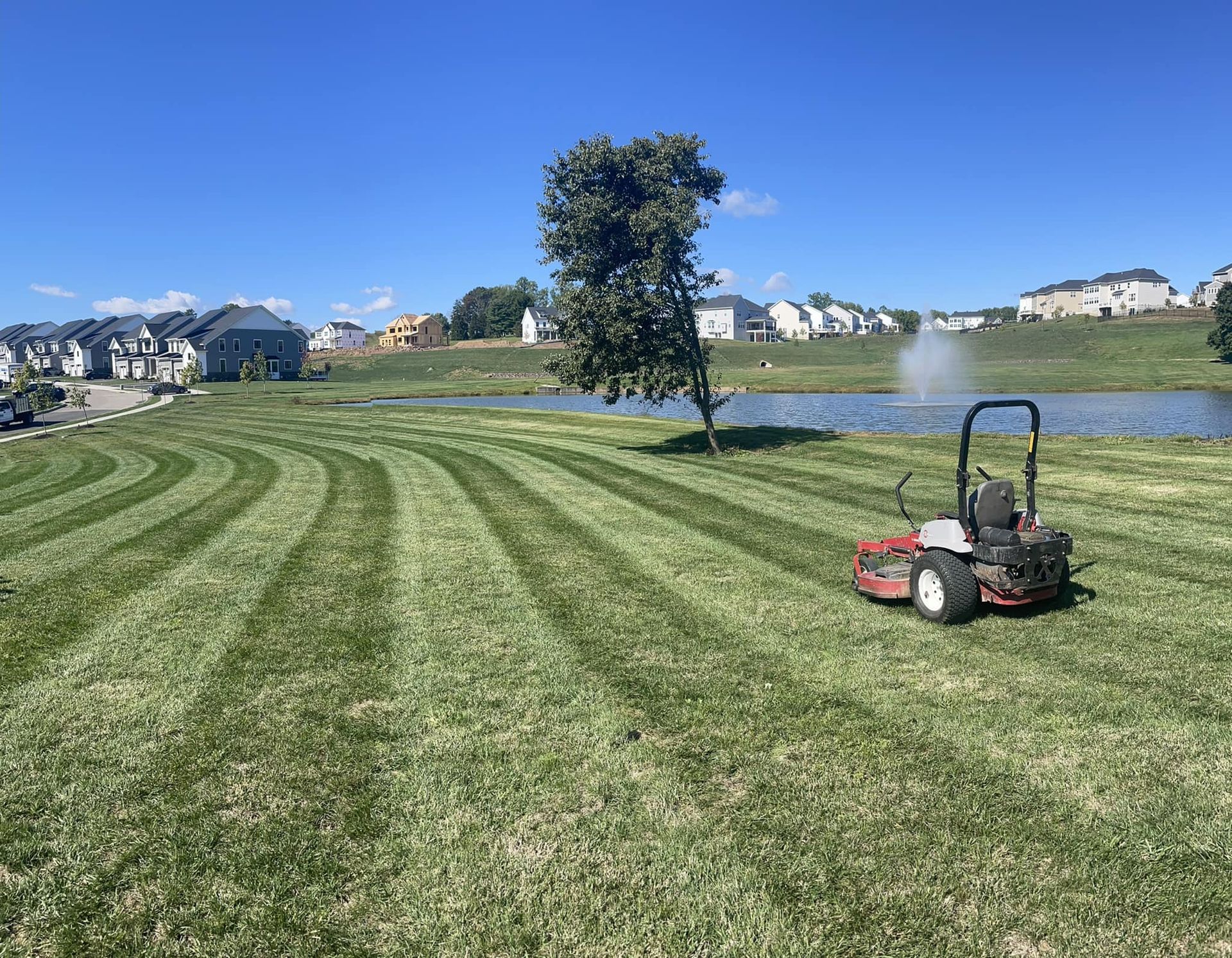 an R&S Property Services riding lawn mower on a freshly cut lawn next to a pond