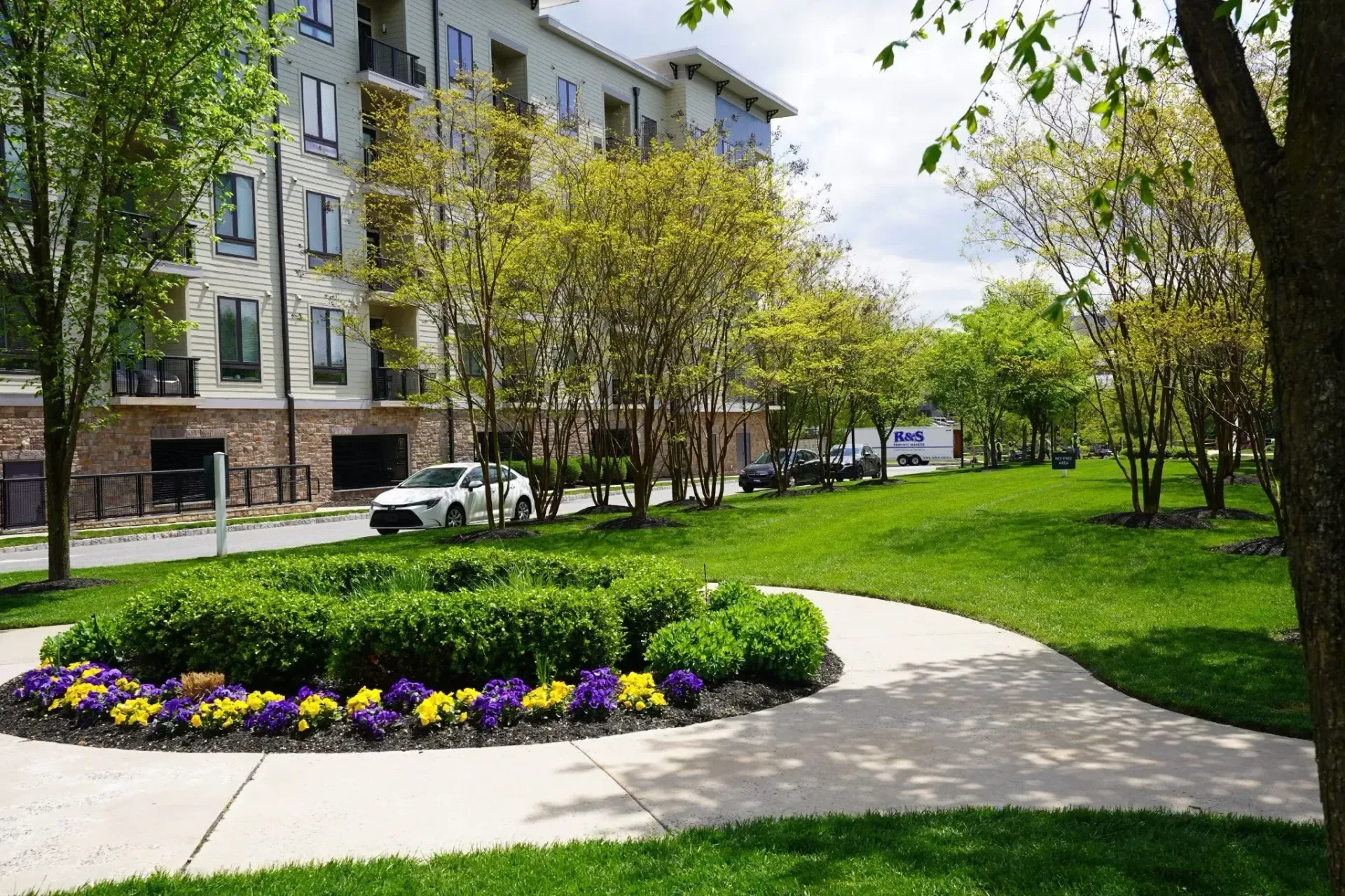 A newly installed landscape design in Chester Springs, PA, featuring new walkways, yellow and purple flowers, shrubs, grass, and trees