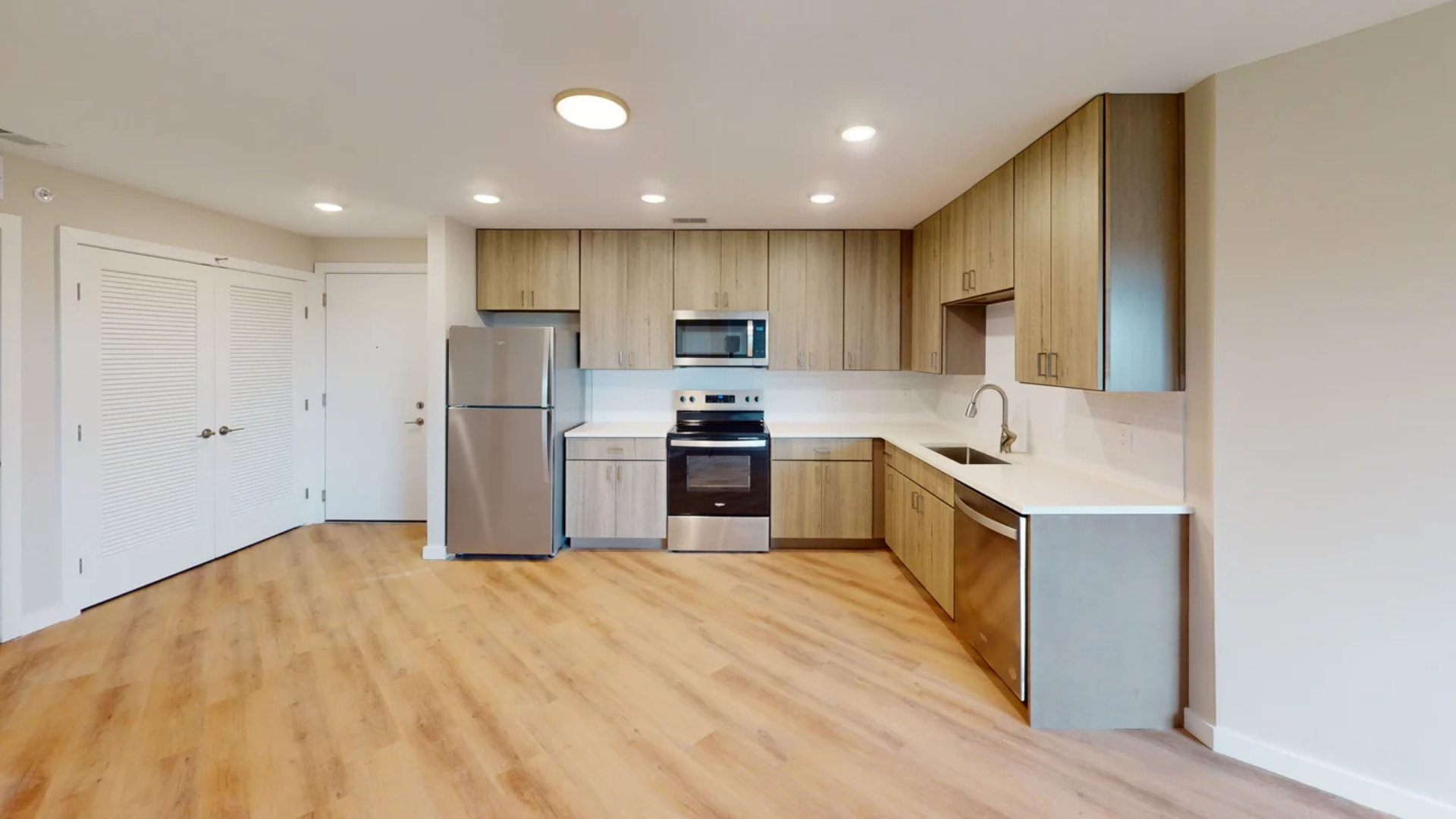 A modern kitchen with light wood cabinets, stainless steel appliances, and white countertops.