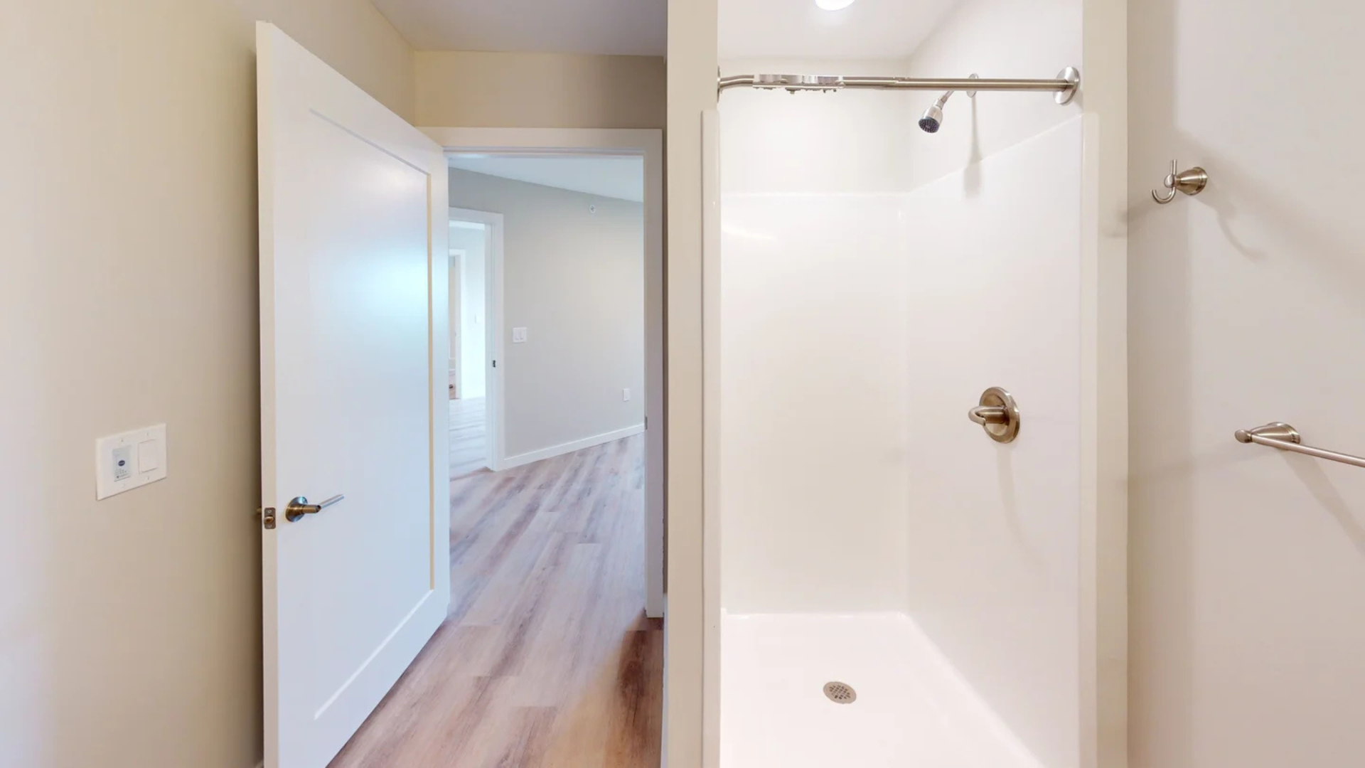 Bathroom with a white shower stall, open doorway to a bedroom with wood floors.
