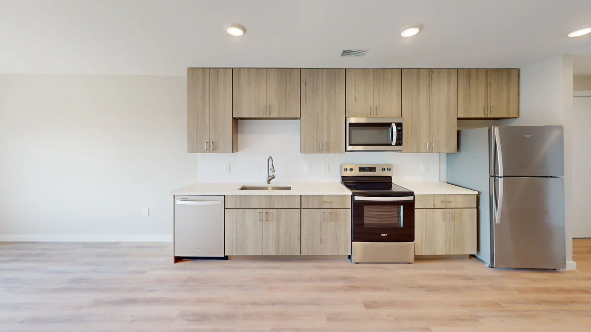 Modern kitchen with light wood cabinets, stainless steel appliances, and white backsplash.