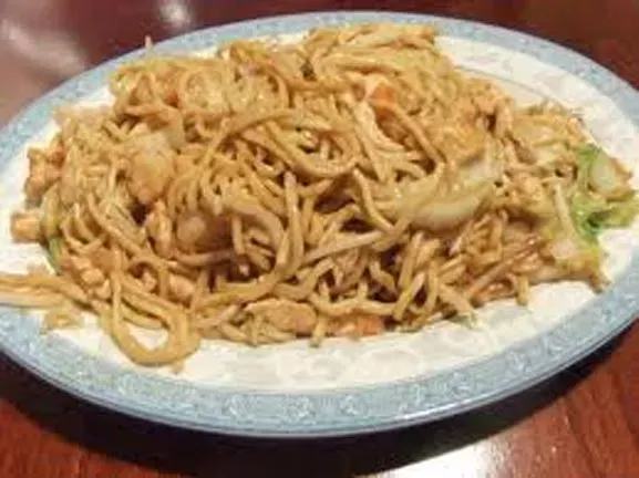 A plate of noodles with chicken and broccoli on a wooden table.