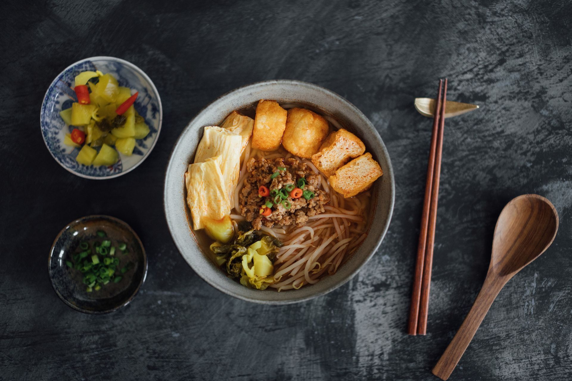 A bowl of food with chopsticks and a wooden spoon on a table.