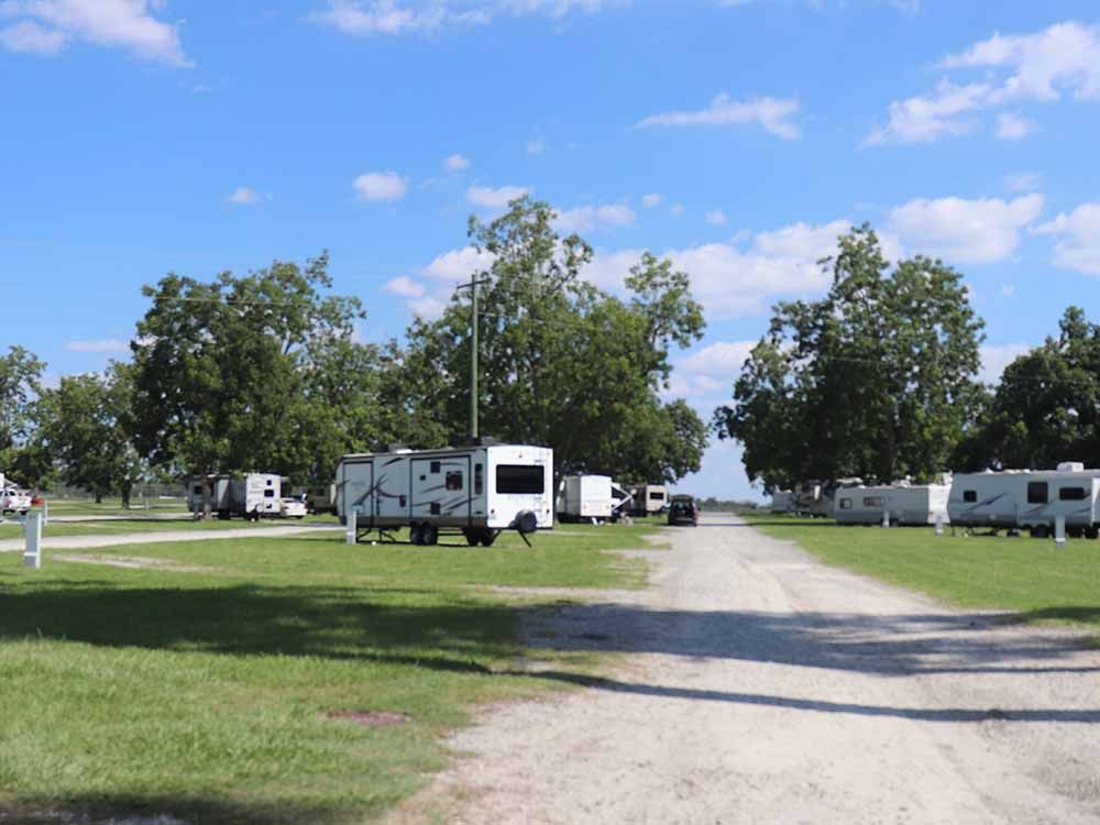 A row of rvs parked in a grassy field next to a dirt road.