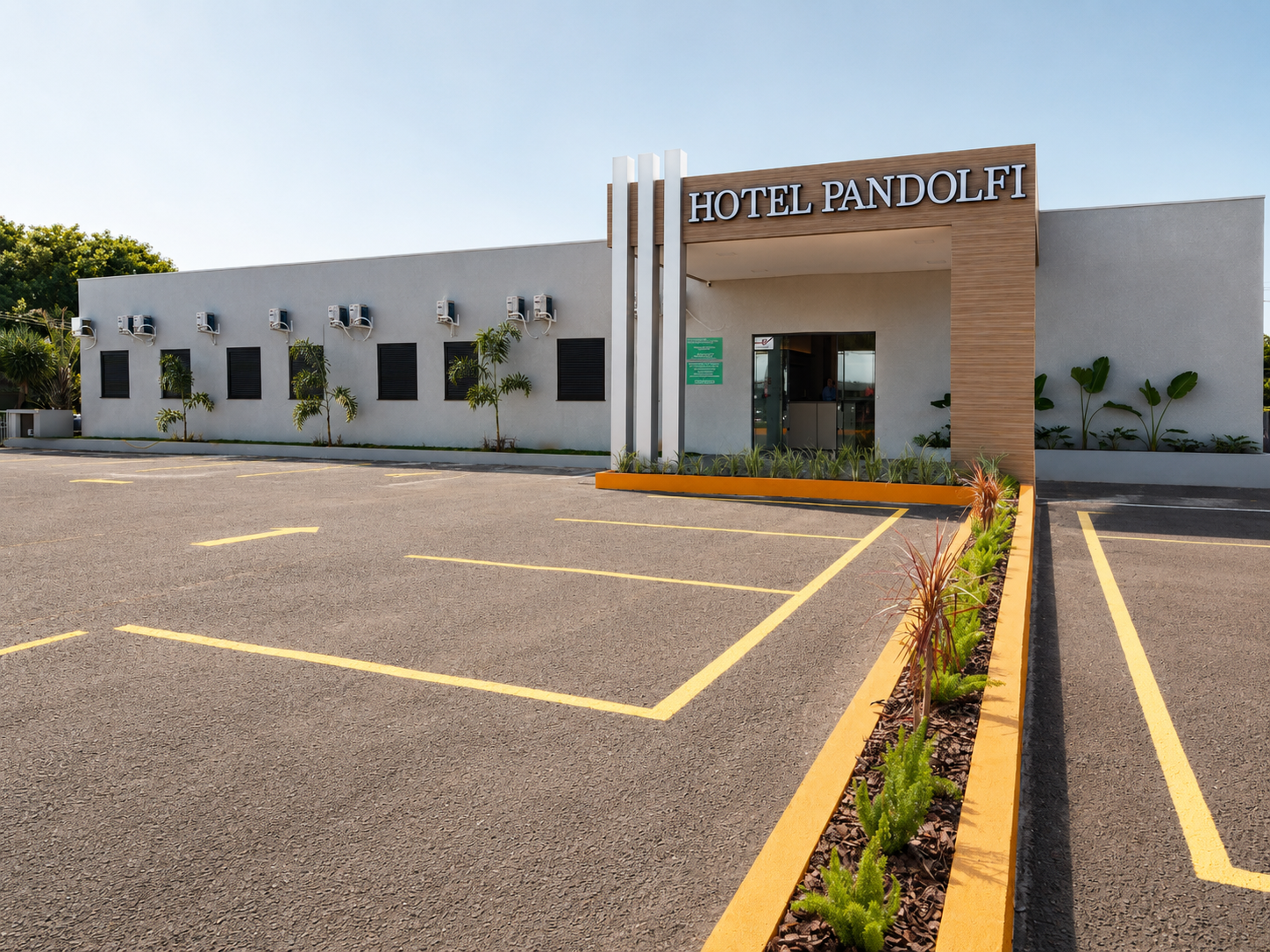 Entrada do Hotel Panduit com estacionamento, fachada branca e bege e faixas amarelas pintadas.