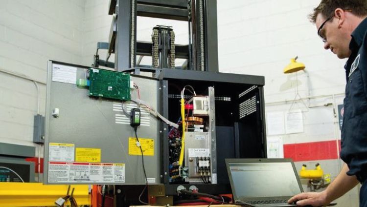 Técnico trabajando junto a un armario de control eléctrico abierto con un ordenador portátil en un laboratorio industrial.