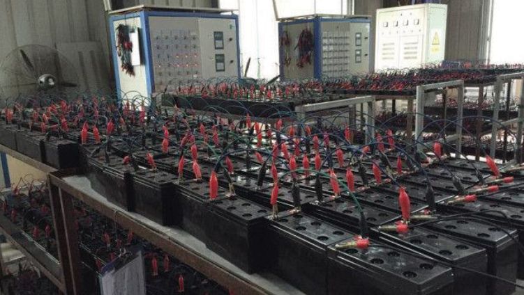 Filas de bancos de baterías con cables rojos en una sala de energía industrial.