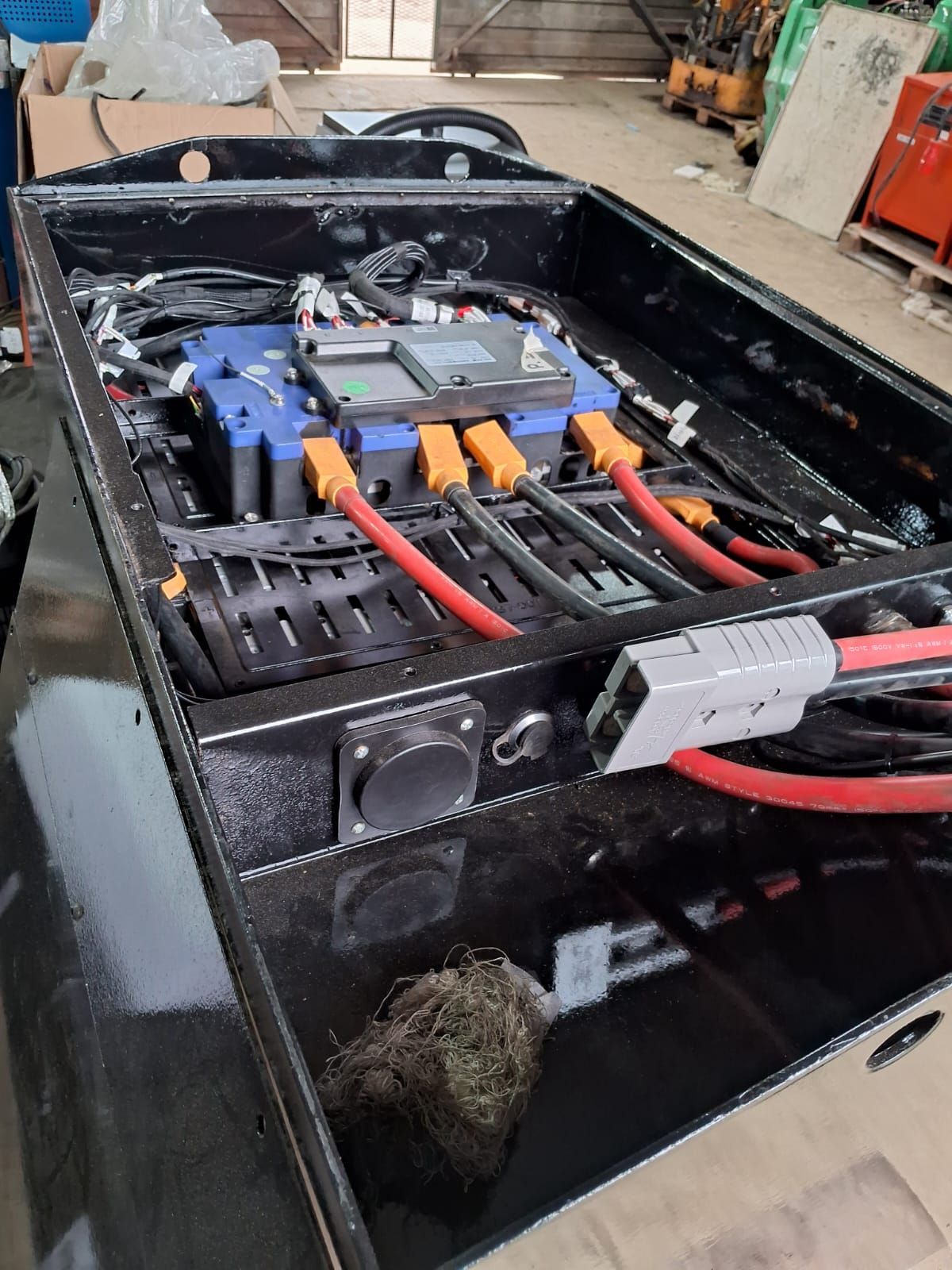 Compartimento de batería negro con cables naranjas y rojos dentro del chasis de un vehículo o maquinaria.