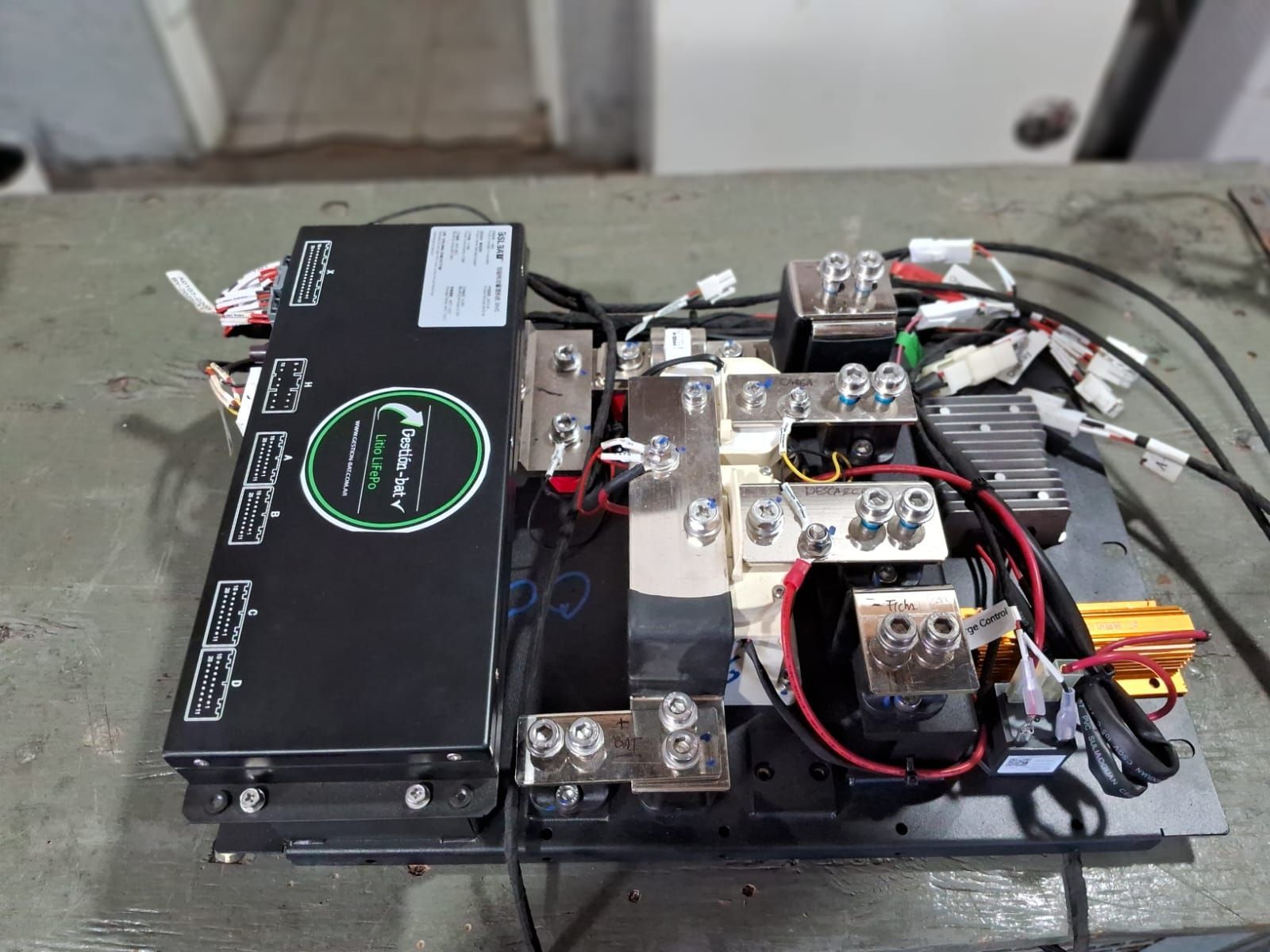 Ensamblaje electrónico abierto con paquete de baterías negro, cableado y componentes metálicos sobre una mesa.