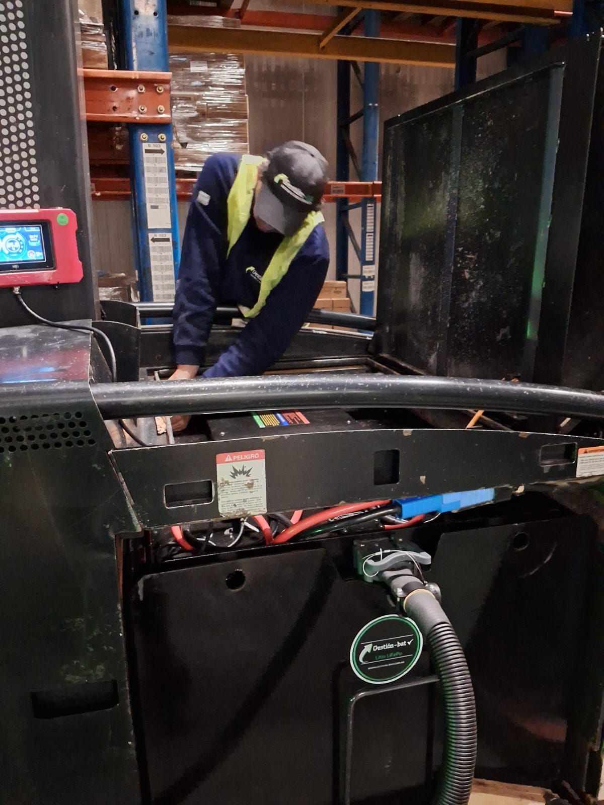 Un trabajador con chaleco reflectante inspecciona la maquinaria en un almacén industrial.