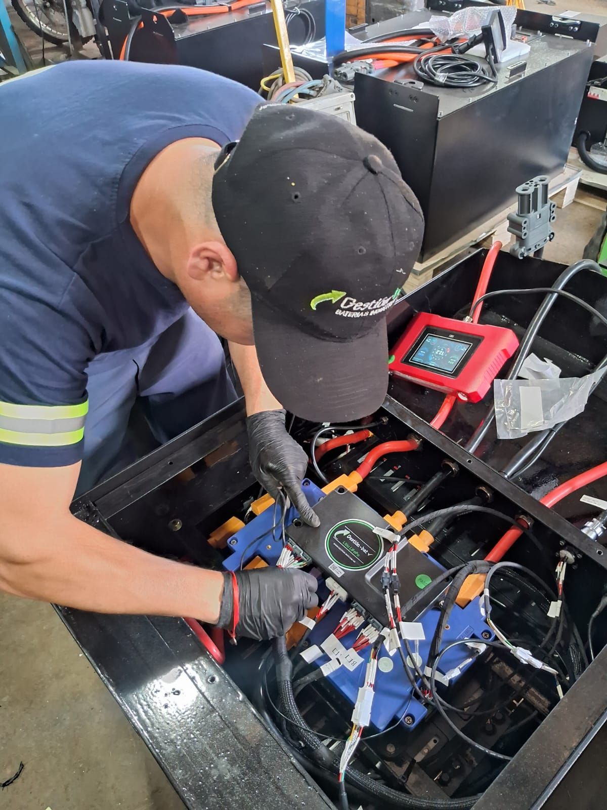 Un técnico con gorro negro inspecciona el cableado eléctrico expuesto dentro de un armario de equipos con un multímetro.