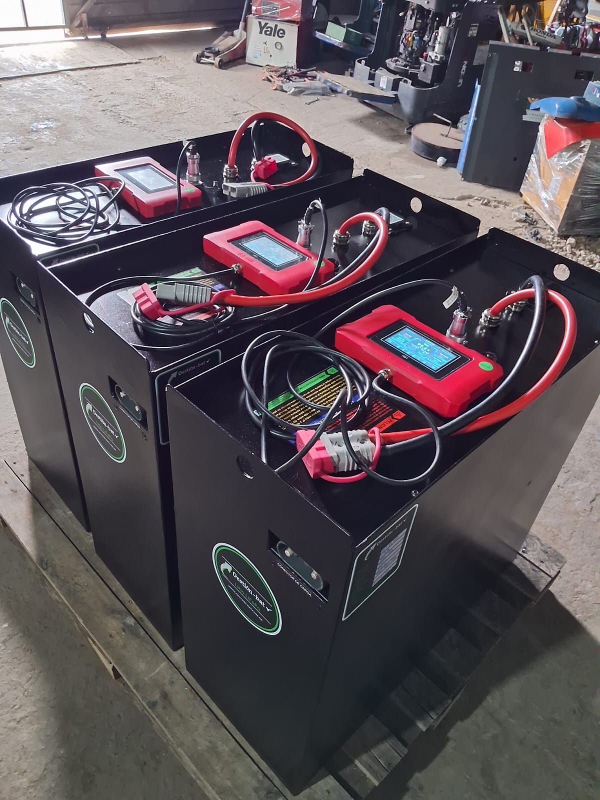 Dos paquetes de baterías negras con dispositivos de diagnóstico y cables rojos en un entorno de taller.