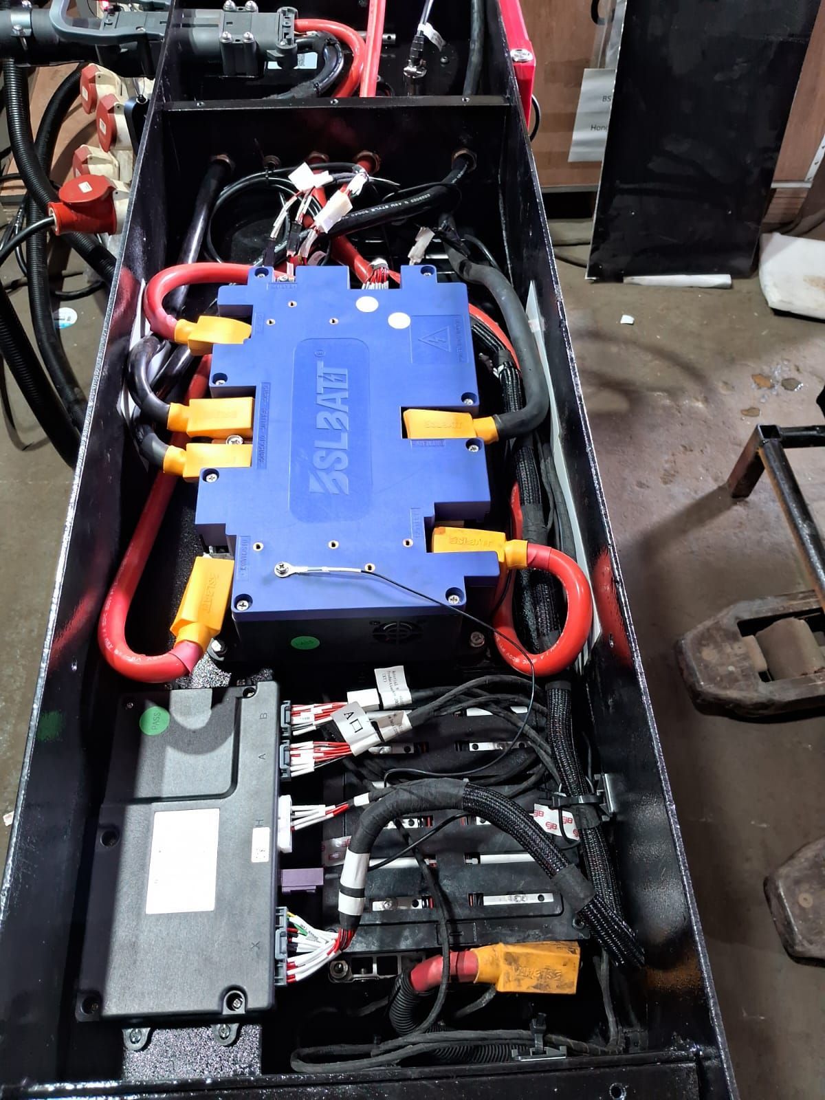 Compartimento de batería abierto con inversor azul y cables rojos dentro de un chasis de vehículo negro.