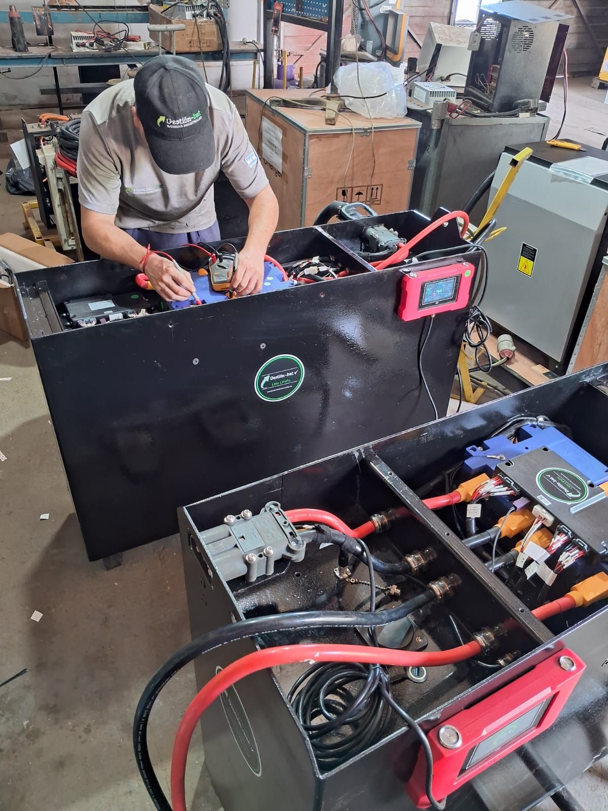 Persona trabajando en un gran paquete de baterías negras con cables rojos en un taller.